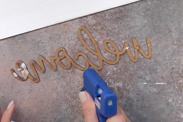 Use low-temp hot glue gun to add glue to the welcome lettering. Then affix to the painted sign, pressing for a few moments to secure.
