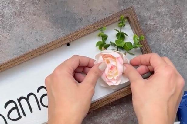 Use a low-temp hot glue gun to affix faux florals and greenery to the painted white sign.