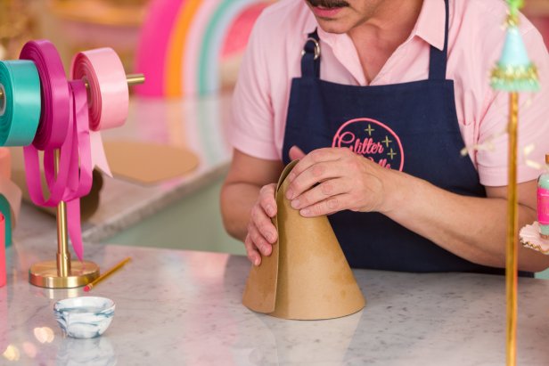 Try this trick to make folding the cardboard into a cone easier: Dip a paper towel into a small dish of water, removing any excess water, then lightly brush over both sides of the cardboard to slightly dampen (Image 1). Then, take two ends of the semi-circle and pull them towards each other to roll the cardboard into a cone (Image 2 + 3). Secure the bottom with a staple (Image 4).