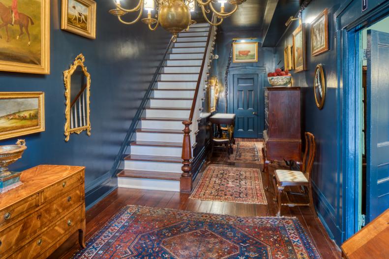 Blue foyer with red area rugs and brass accents. 