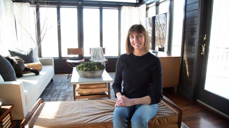 Woman Sits on Leather Sofa in Dark Panel Sunroom Smiling to Camera