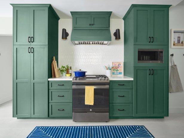 This modern kitchen features emerald green cabinets, white picket tile backsplash and a navy blue washable rug.