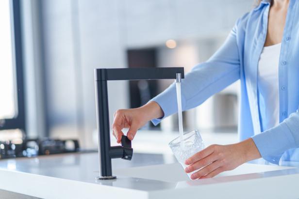 Female pours fresh filtered purified water from a tap into a glass at kitchen at home