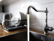 Water flowing out of a kitchen stainless steel tap into the sink. Wasting water by leaving a chrome faucet tap running. Overusing household water. Water misuse in domestic duties and activities.