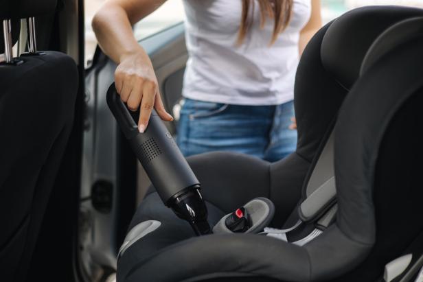 Close-up of female using portable vacuum cleaner in her car. Baby ca seat cleaning. Woman vacuuming seats. Dust and dirt removal