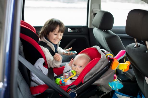 Little baby boy and his older brother, traveling in car seats, going on a holiday, preschool boy playing with mobile phone