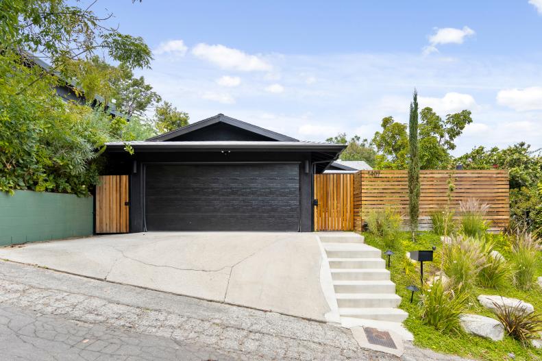 View of driveway leading to black garage door with redwood fence 