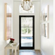A Narrow Entryway With a Glass Front Door and Interesting Light Fixture