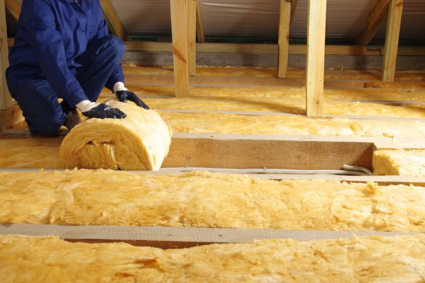 Construction worker thermally insulating house attic with glass wool 