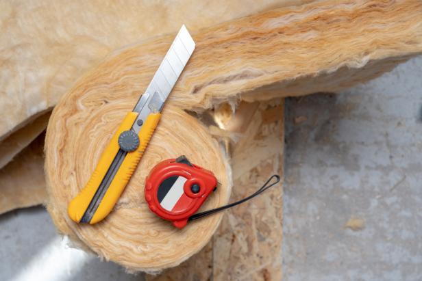Top view of mineral rockwool lying on attic floor inside house under construction with construction knife and measure type equipment