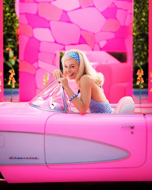 Blonde woman looks over the windshield of pink car.