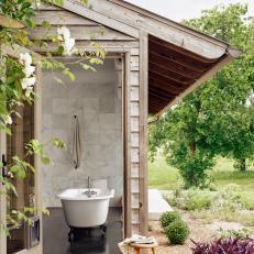 A Rustic Outbuilding Showcases Neutral Tile and a Clawfoot Tub