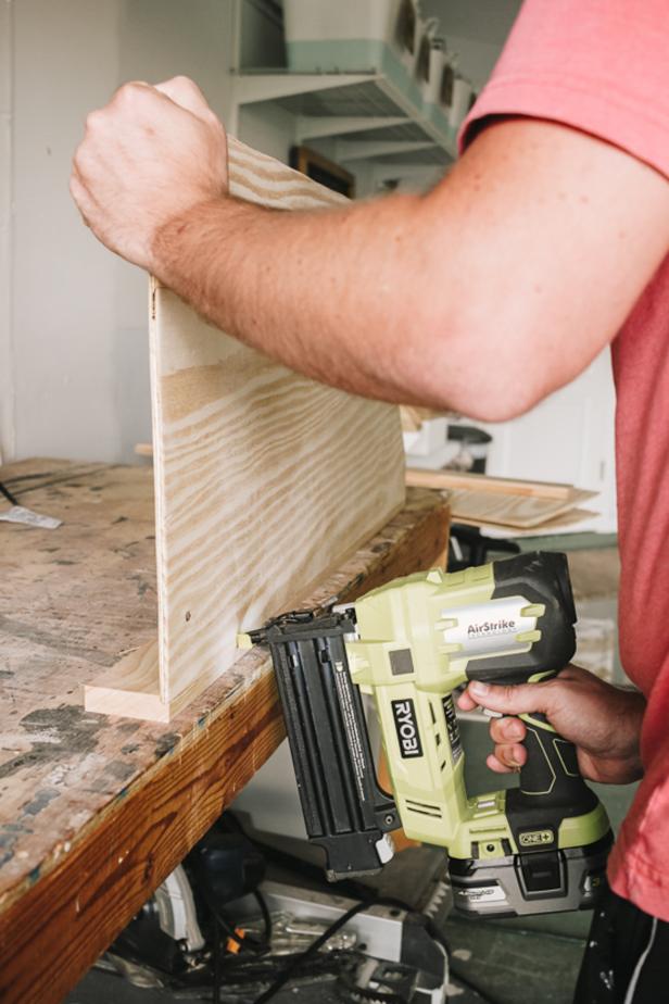 Man nailing plywood to pine wood piece using a brad nailer 