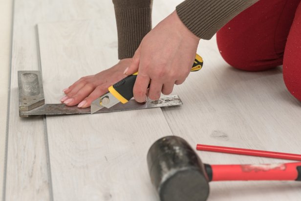 Female master cuts quartz vinyl floor with a stationery knife, floor installation, woman performs repair work.