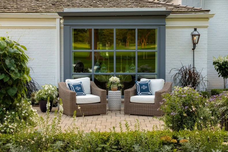 A Daytime Moon Garden A small backyard patio with two chairs, a side table, evergreen shrubs and plants in shades of white and pastels.