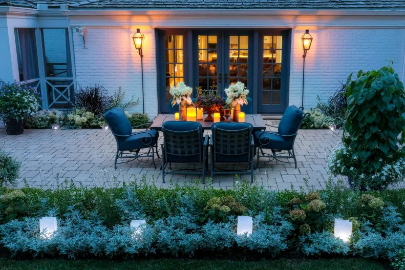 A Moon Garden for a Small Backyard A small backyard patio with two chairs and side tables and a border of evergreen shrubs and plants that reflect moonlight.