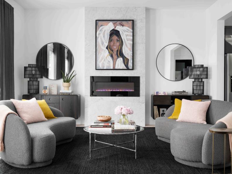 A sleek electric fireplace with white Carrara marble surround adds a stylish focal point, and brings warmth and comfort to this chic space. A vintage brass side table by one of the two curved sofas has a coordinating kidney shape.