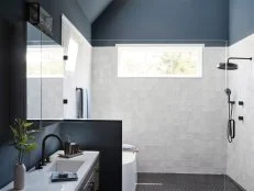A strong horizontal window in the shower brings light into the space while still maintaining privacy. A glass partition keeps the shower space feeling open while white porcelain tile in a marble finish adds stylish luxury to morning showers.