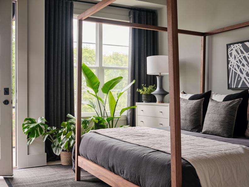 The main bedroom at HGTV Urban Oasis 2022 provides a relaxing retreat with neutral, understated tones of white and gray against wood accents and layered botanicals.