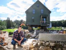 Jonathan Knight in front of his lifted New England farmhouse, prior to it being moved down the road, as seen on Farmhouse Fixer.