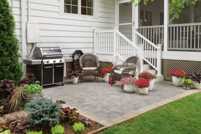 Design Your Yard for Grilling A small, paved area in a backyard with a grill and a few outdoor chairs.