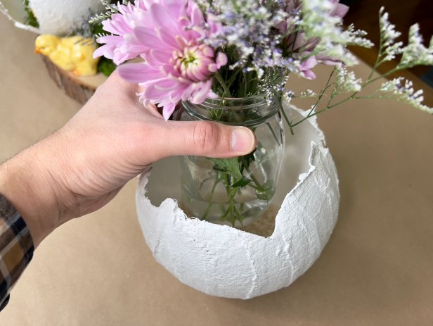 Add dry rice, beans or small rocks to the inside of the egg to keep it from rolling or tipping over. Find a jar or vase that is small enough to fit inside the egg without being seen. Make sure to cut the flowers long enough, so they pop out of the egg. Arrange them in the jar or vase and fill the water half way. Place the flowers in egg and arrange with other eggs and easter embellishments.