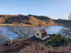 A tiny house cabin perched on a hill above a lake in Scotland