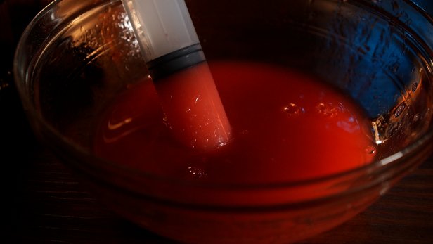 First add 2-1/2 cups of room temperature water to a mixing bowl. Turn on the electric mixer and slowly add in 1 teaspoon of sodium alginate powder to the bowl. Tip: The alginate powder will clump up, so keep mixing and increasing the speed until the mixture is dissolved and a thick, viscus liquid is produced. Next, add red food coloring to make organ-like specimens. Stir the mixture together with a wooden spoon. In a glass cup, add 2-1/2 cups of cold water and 2 tablespoons of calcium chloride and mix with a wooden spoon until dissolved. Tip: The longer you let the mixture sit after its dissolved, the clearer the water will become. Use a plastic syringe to extract the red dyed sodium alginate mixer.