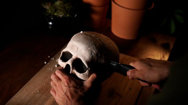 Use a serrated knife to cut a foam or plastic skull in half to minimize depth. Use a low temp hot glue gun to affix the skull to the center of the frame.