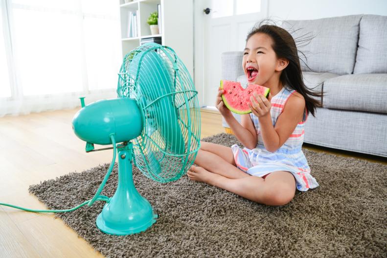 girl holding watermelon sitting in front of electric fan