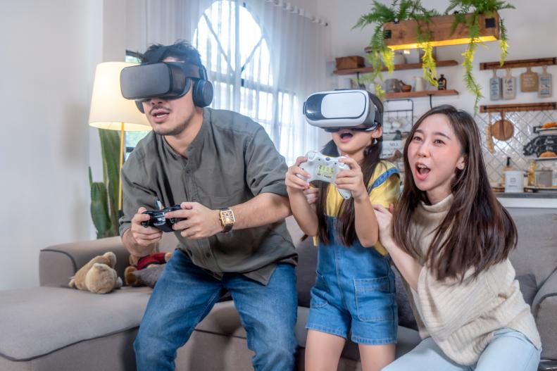 Cheerful family playing virtual reality headset with controller gamepad playing racing video game at home.