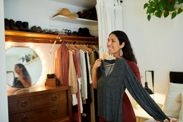Smiling woman choosing a dress to wear while standing by a closet in her bedroom at home