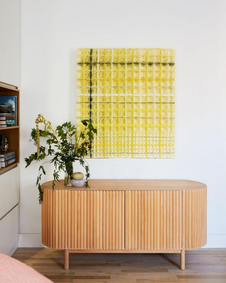 A photo of a yellow woven art piece and a wooden credenza. 