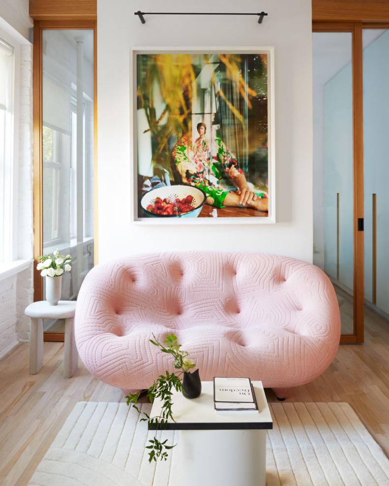 A photo of a living room with colorful art and a chic, pink sofa.