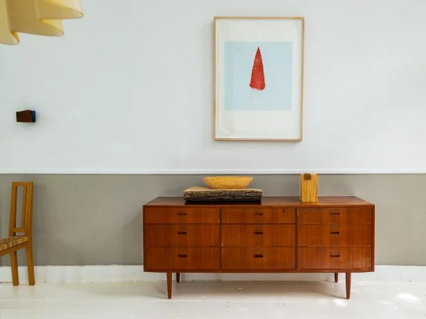 White room with grey lower half and warm wood credenza below art.
