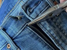 Removing the zipper stop from jeans with a pair of pliers.