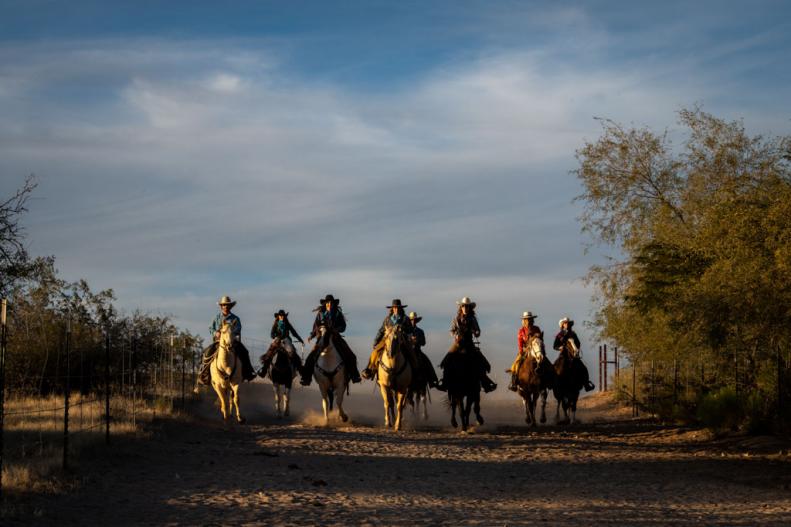 People riding horses down a desert trail with a blue sky and clouds in the background