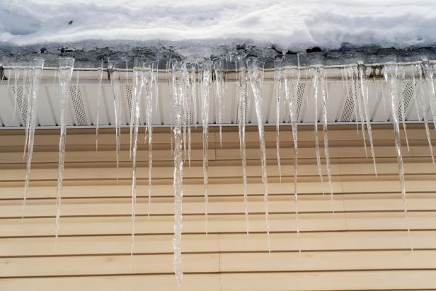Sharp spiked icicles on roof with snow. Icicles on roof of private house resulting from improper construction of roof. 