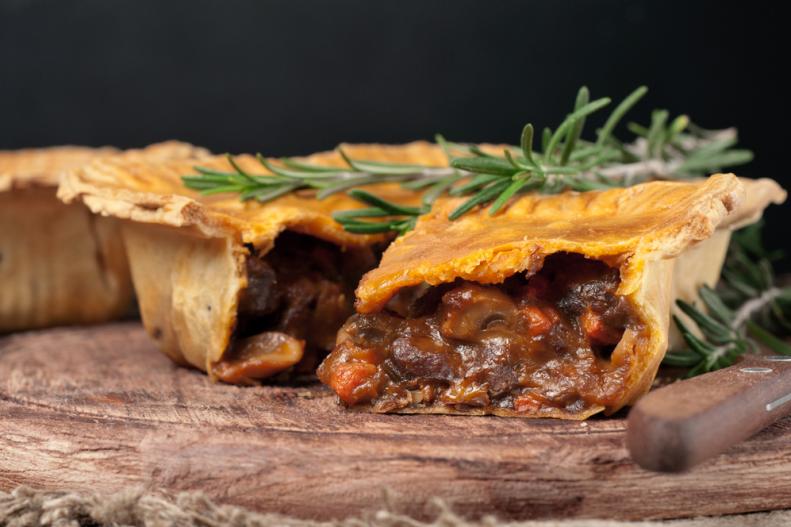 A close-up of an Australian meat pie on a rustic wooden table