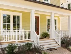 Front view of a yellow house with white porch railing. 
