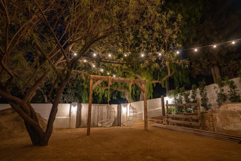 An outdoor living space with string lights and two hanging chairs to swing in.
