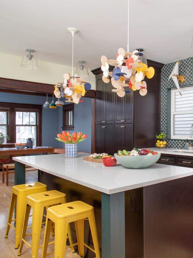 This blue kitchen from HGTV Magazine features colorful statement lighting, fish scale backsplash tiles and yellow bar stools.