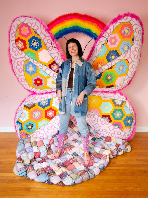 A woman stands in front of a brightly-colored butterfly rainbow prop.