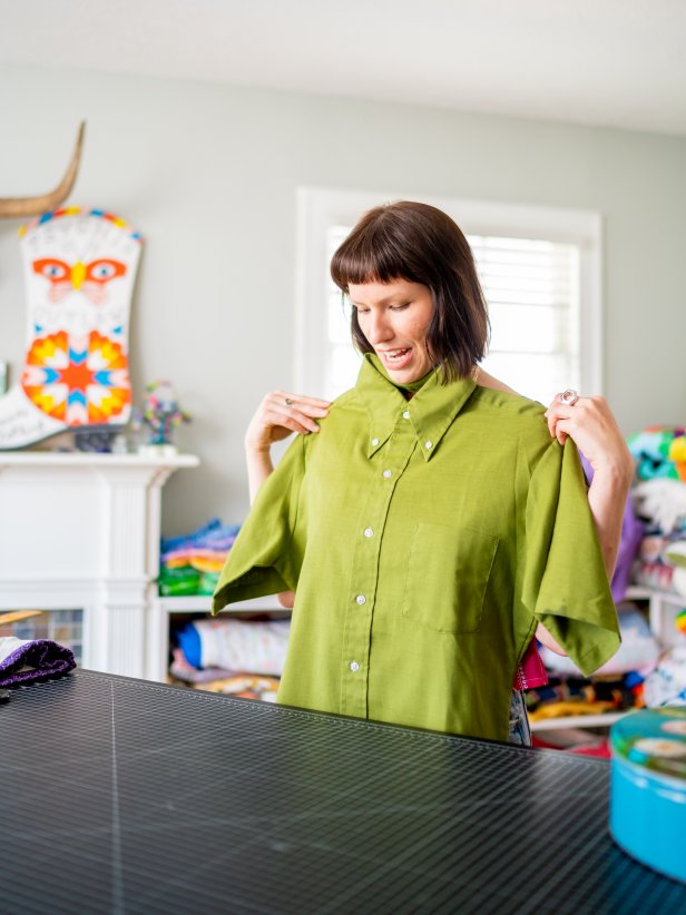 A woman holds up a men's vintage button-down shirt. 