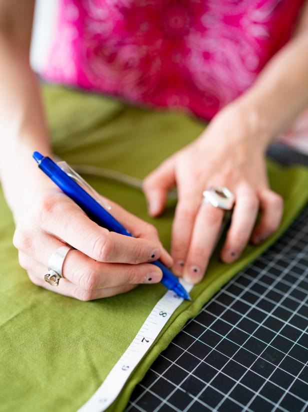 A woman marks on a green shirt with a blue heat pen. 