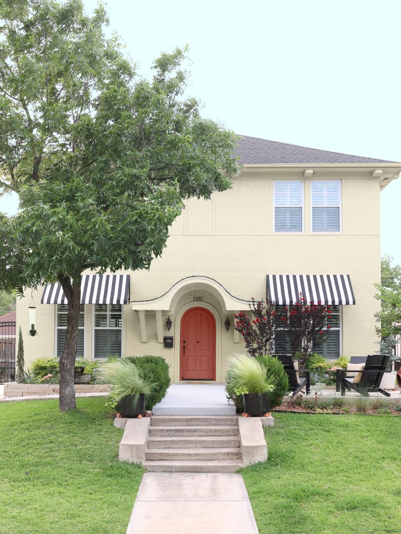 This painted brick home from HGTV Magazine features painted brick, a pink arched door and striped awnings.