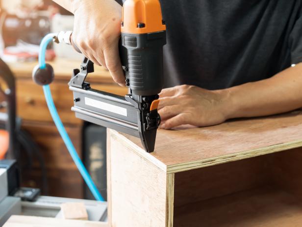 carpenter using nail gun or brad nailer tool on wood box in a workshop ,furniture restoration woodworking concept. selective focus