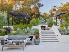 A sofa and coffee table on a patio and steps leading to an upper terrace with a dining table, outdoor bar and fireplace.