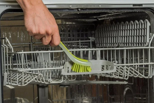 A man's hand brushes a dishwasher machine