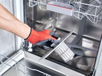 Concept maintenance service of home appliances. Worker cleans filter in dishwasher. Male repairman checking food residue filters.